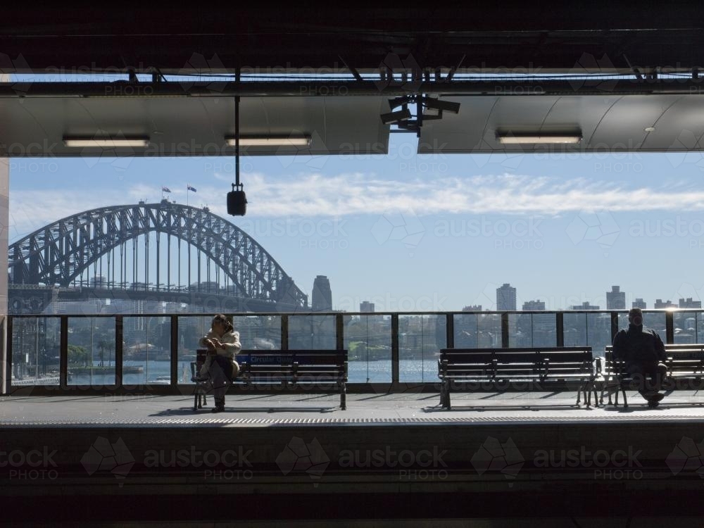 Two people waiting at Circular Quay Railway Station with the Harbour Bridge in the background - Australian Stock Image