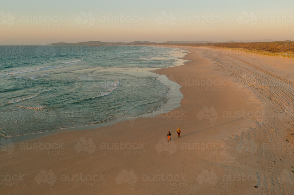 Two people walk along the beach in the soft morning light - Australian Stock Image