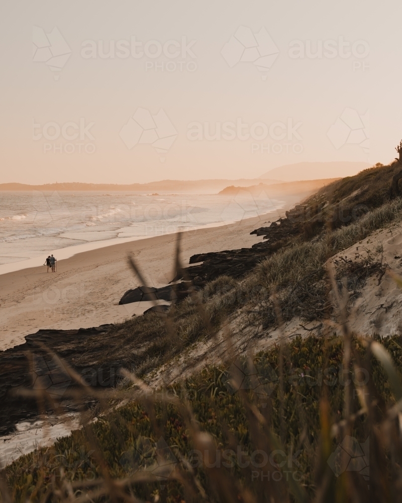 Two people walking along a deserted beach at sunset. - Australian Stock Image