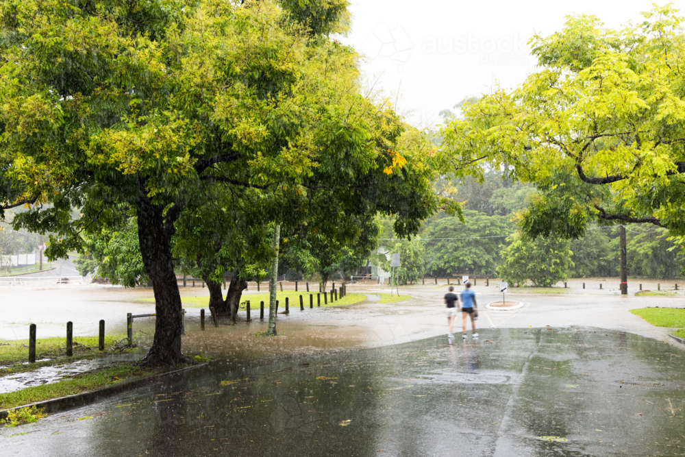 Image of Two people walking along a flooded street in suburban Brisbane ...