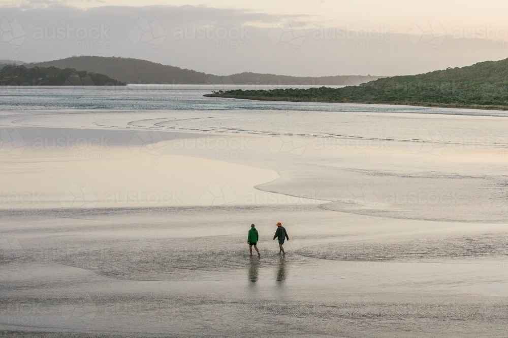 Two people walking in the shallow water of an inlet on a winters day - Australian Stock Image