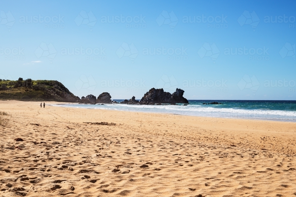 Two people walking on beach towards Camel Rock - Australian Stock Image