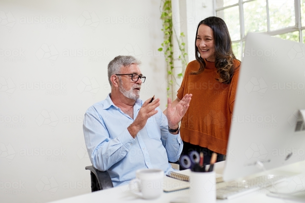 Two professional business people, sharing ideas in an open-plan studio office - Australian Stock Image