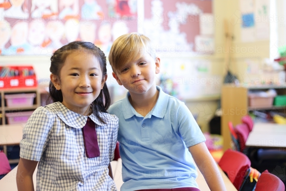 Two school aged children sitting on desk in classroom - Australian Stock Image