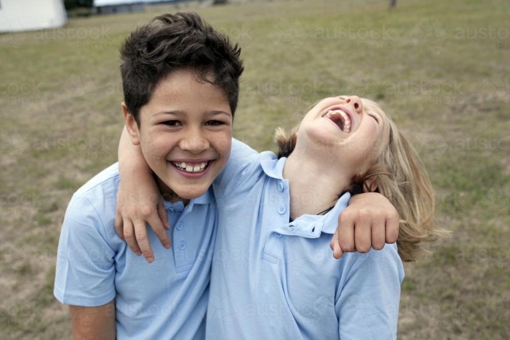 Two school kids laughing outside with arm around each other - Australian Stock Image