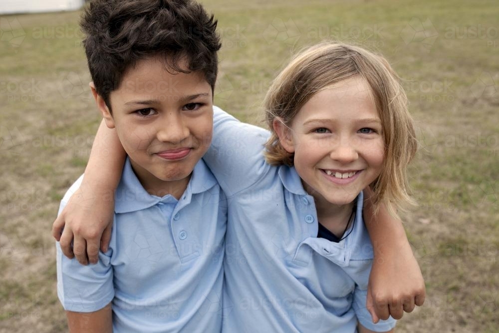 Two school kids outside with arms around each other - Australian Stock Image