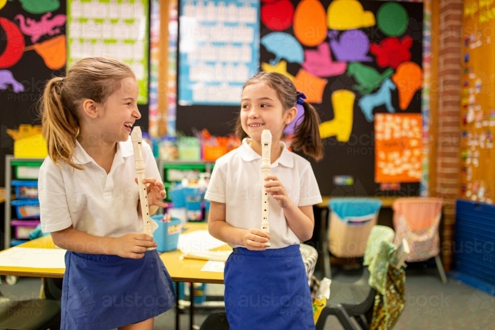 Two Schoolgirls Laughing in Classroom playing Recorders - Australian Stock Image