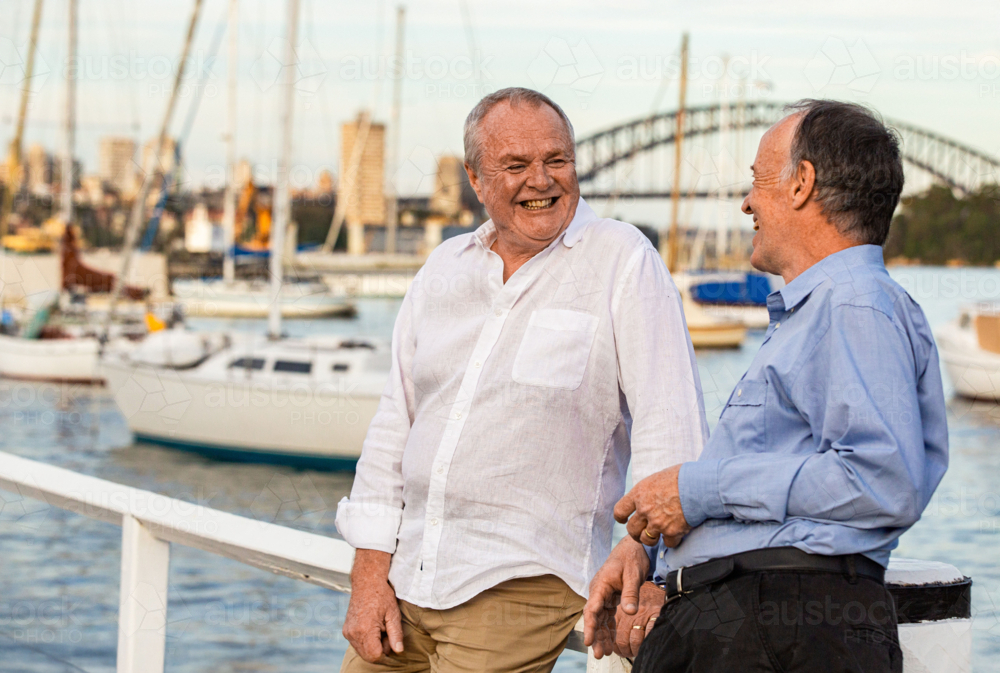 Two senior men standing and leaning against the wooden rails at the pier - Australian Stock Image