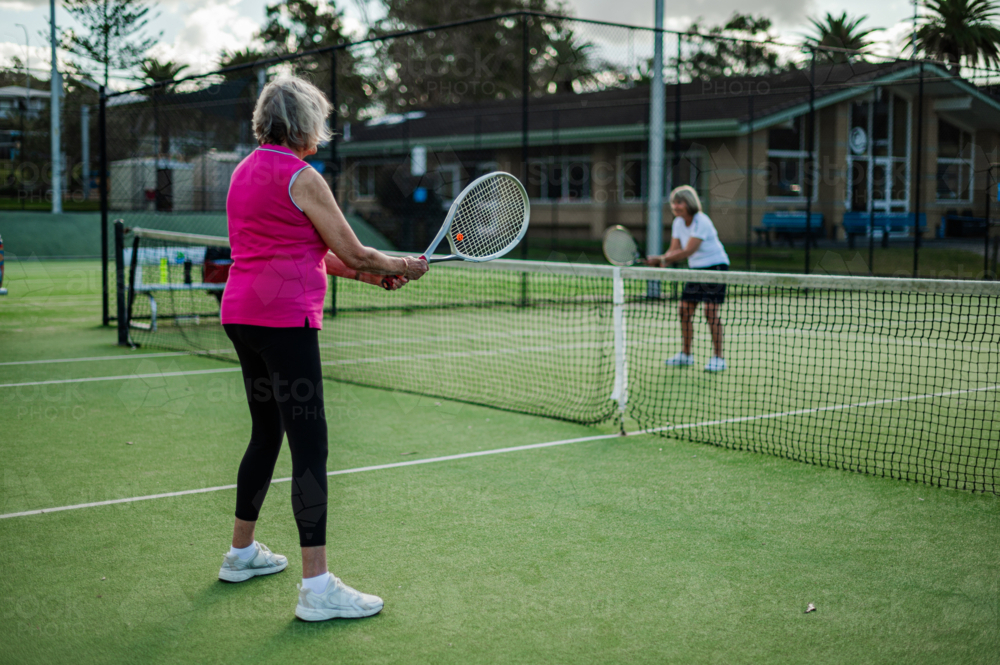 Two senior women engaged in a friendly tennis match at a community facility outdoors - Australian Stock Image