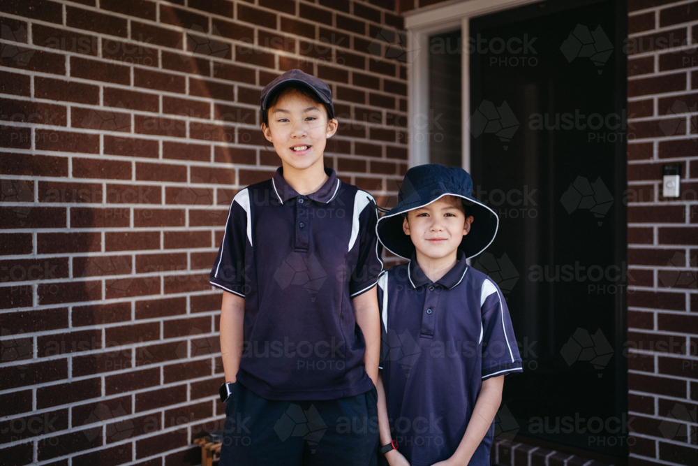 Two siblings standing outside of their house in uniform ready for school - Australian Stock Image