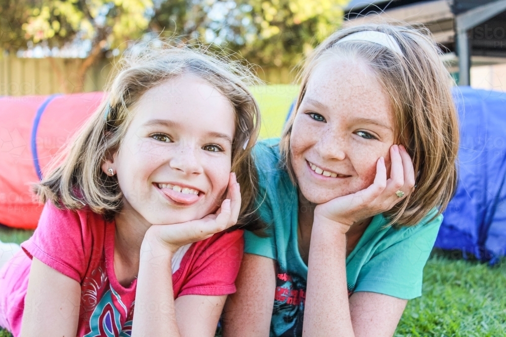 Two sisters resting head on hand smiling poking tongue out - Australian Stock Image