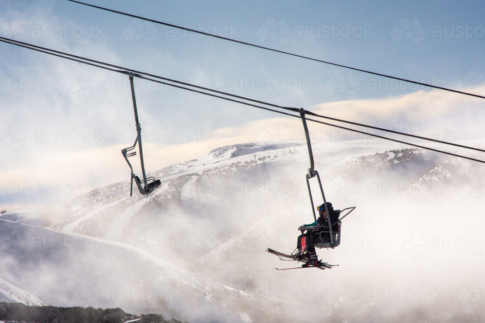 Two skiers on chairlift with misty mountains in background - Australian Stock Image