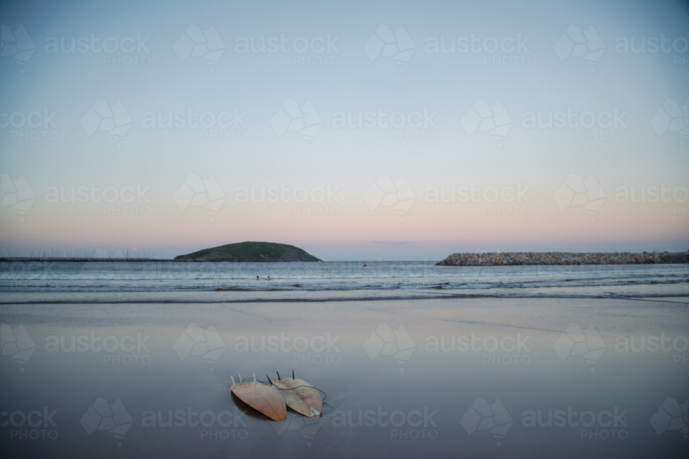 Two surfboards on the beach at twilight with kids swimming in the distance. Coffs Harbour, NSW - Australian Stock Image