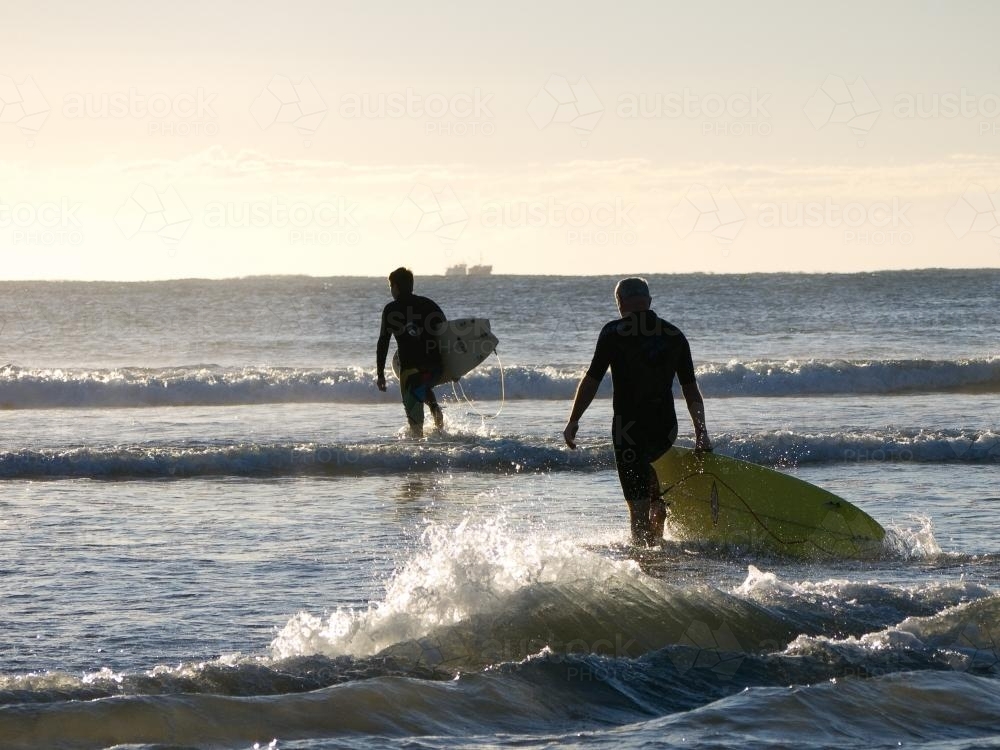 Two surfers entering the water in the early morning light - Australian Stock Image