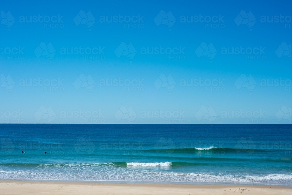 Two surfers waiting for a wave on a flat beach - Australian Stock Image