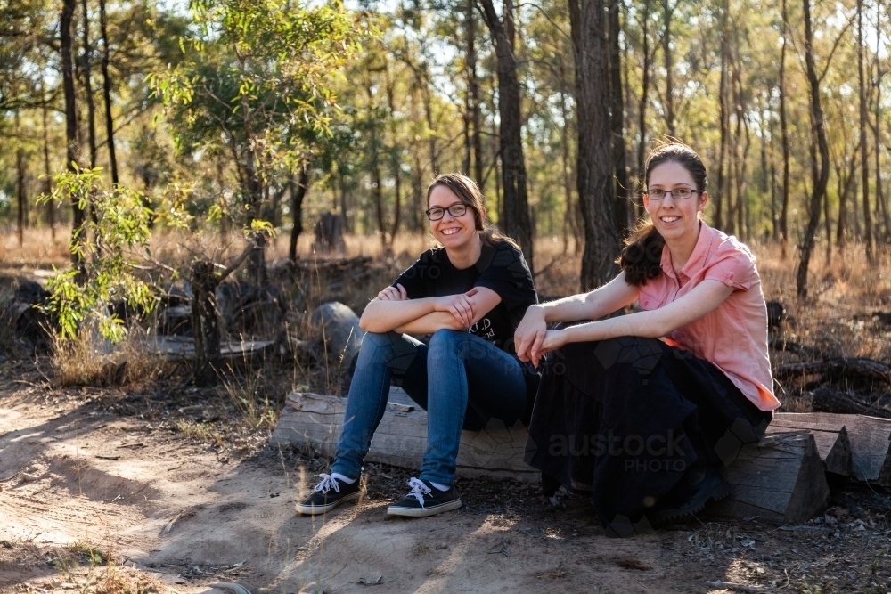 Two teen girls sitting on log in paddock - Australian Stock Image