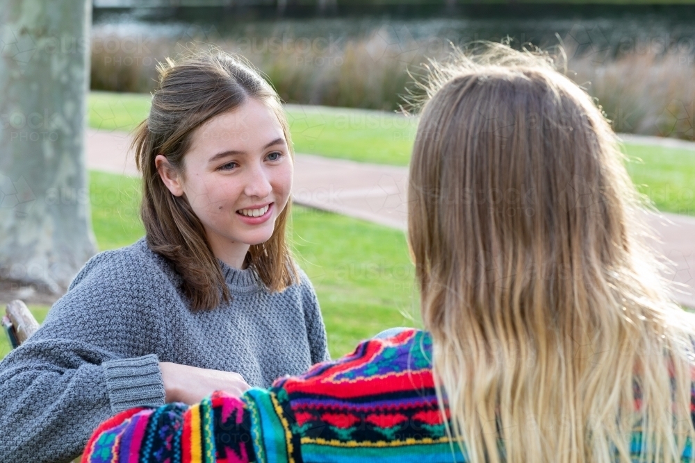 two teen girls sitting on park bench together - Australian Stock Image