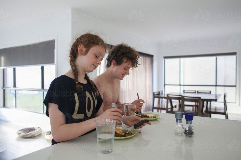 Two teenage children eating breakfast at home - Australian Stock Image