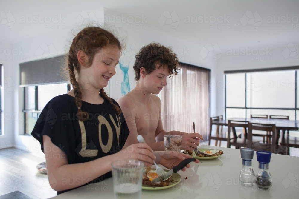 Two teenage children eating breakfast at home - Australian Stock Image