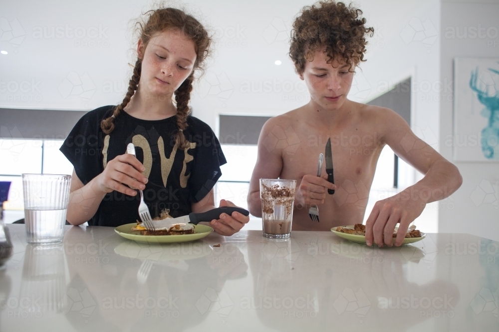 Two teenage children eating breakfast at home - Australian Stock Image