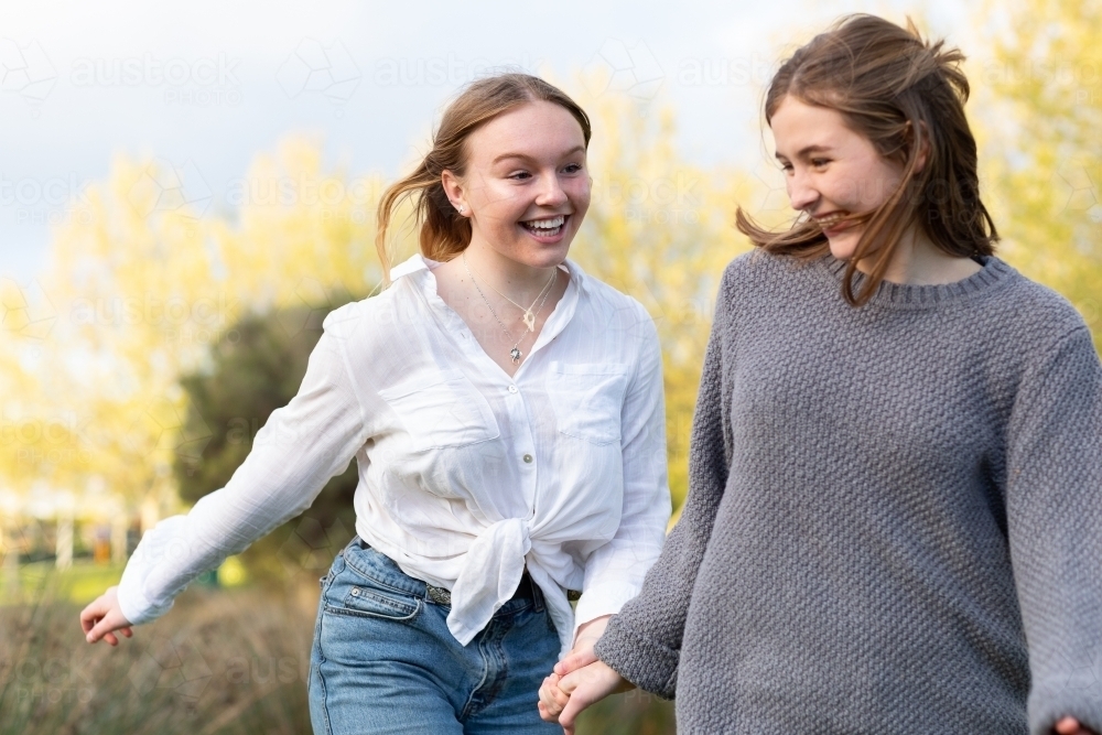 two teenage girls holding hands in natural setting - Australian Stock Image