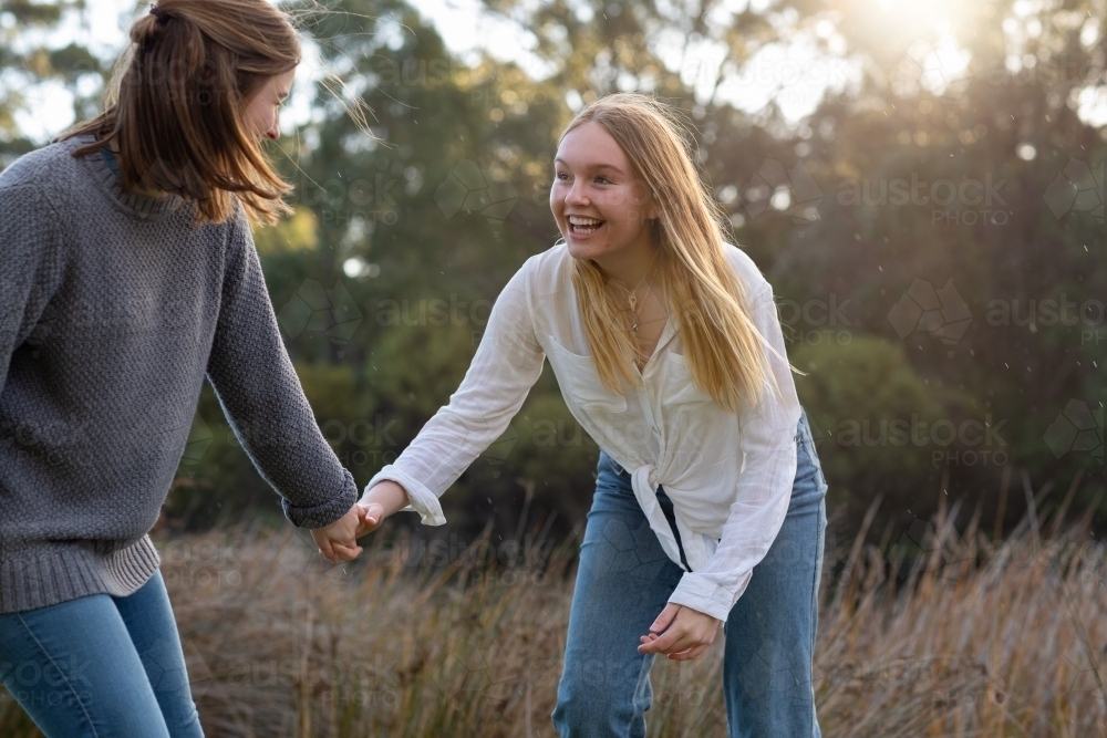 two teenage girls holding hands in natural setting - Australian Stock Image