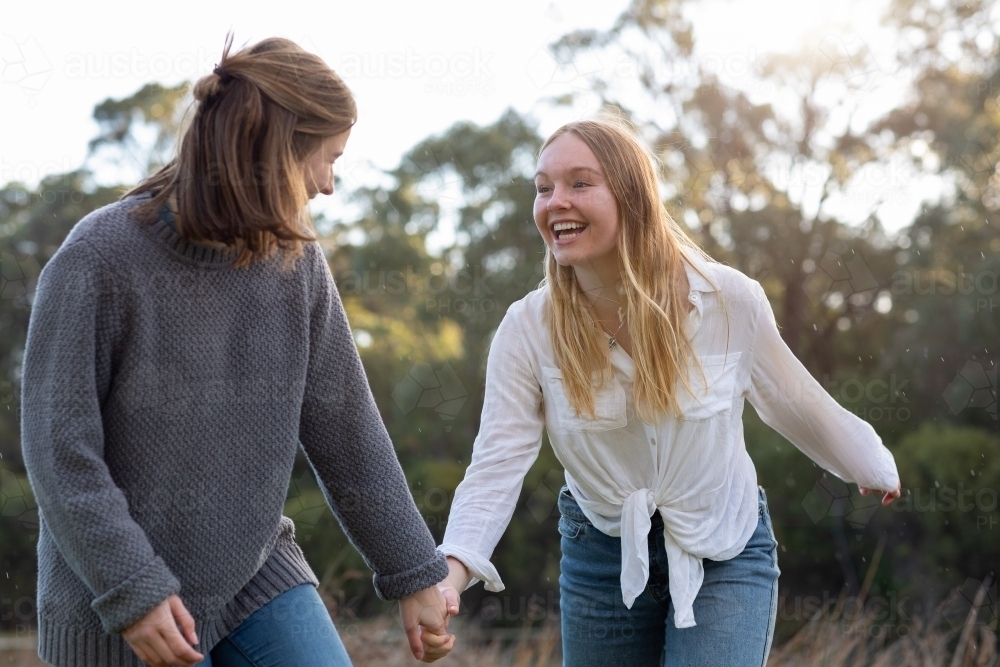 two teenage girls holding hands in natural setting - Australian Stock Image