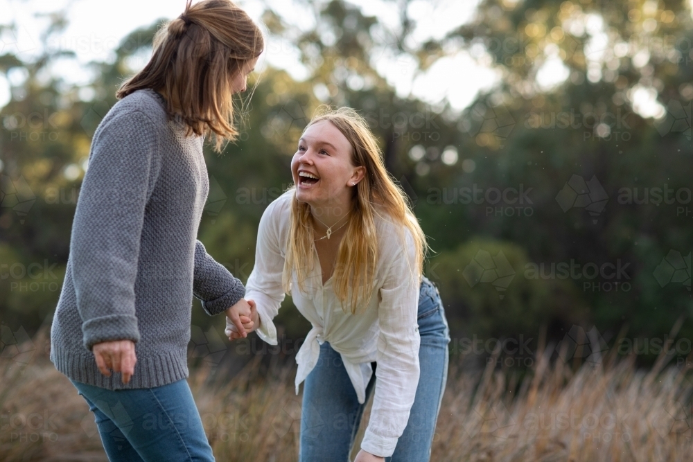 two teenage girls holding hands in natural setting - Australian Stock Image