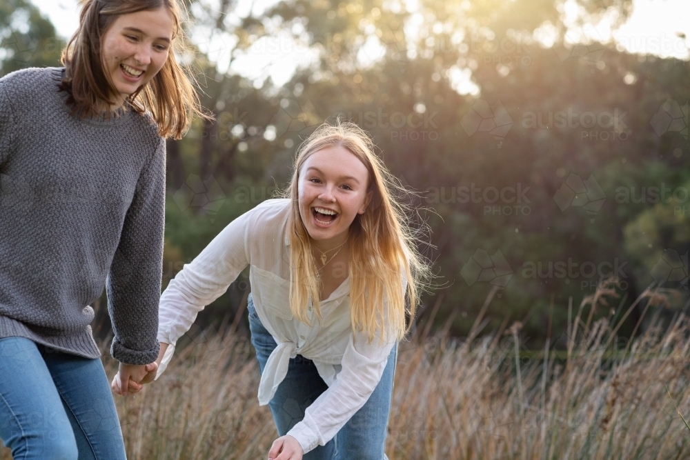 two teenage girls holding hands in natural setting - Australian Stock Image