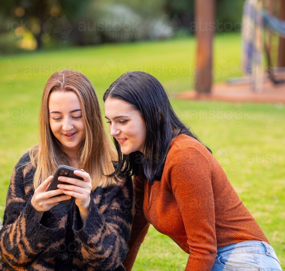 two teenage girls sitting outside looking at smartphone - Australian Stock Image