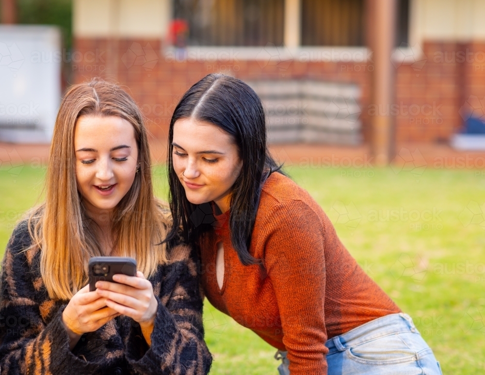 two teenage girls sitting together and looking at smartphone - Australian Stock Image