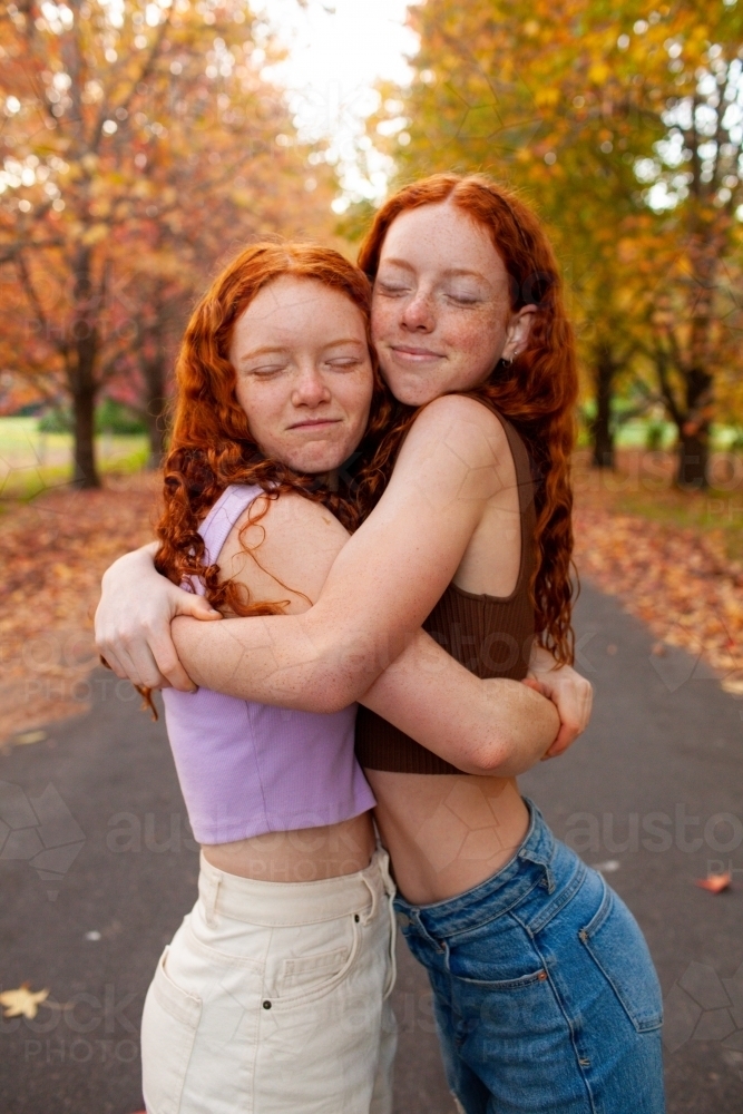 Two teenage girls standing in a street lined with Autumn trees - Australian Stock Image