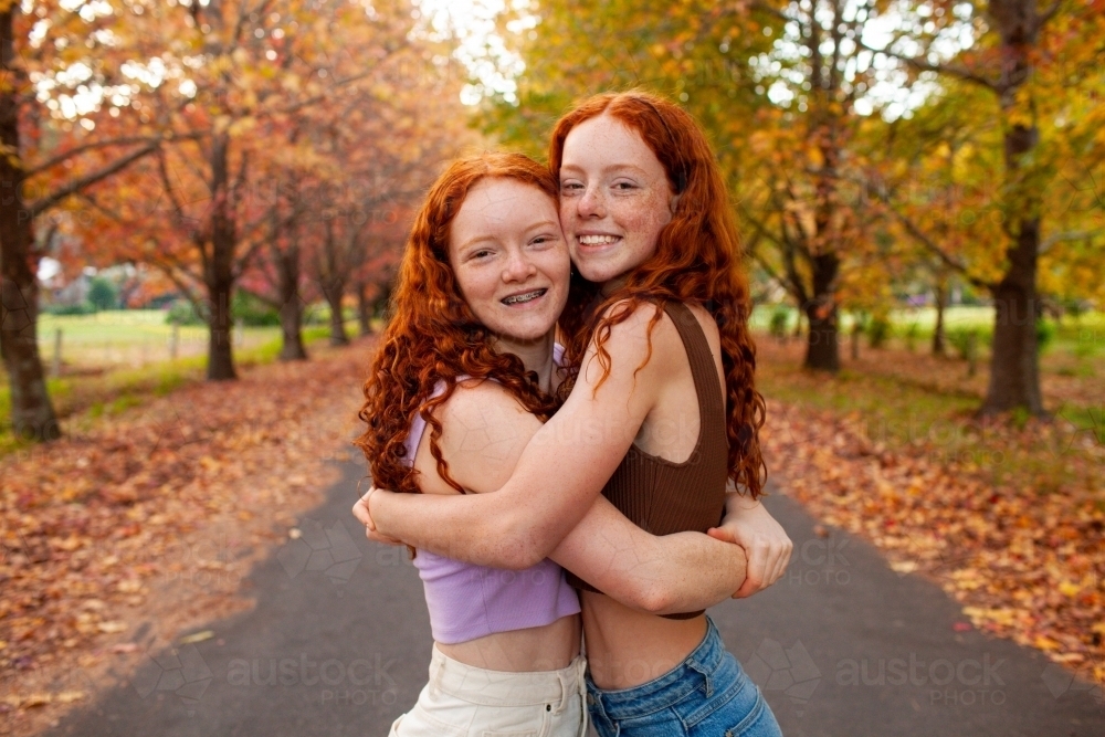 Two teenage girls standing in a street lined with Autumn trees - Australian Stock Image