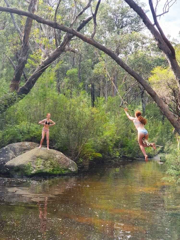 Two teenage girls swinging on a rope swing at a rock pool - Australian Stock Image