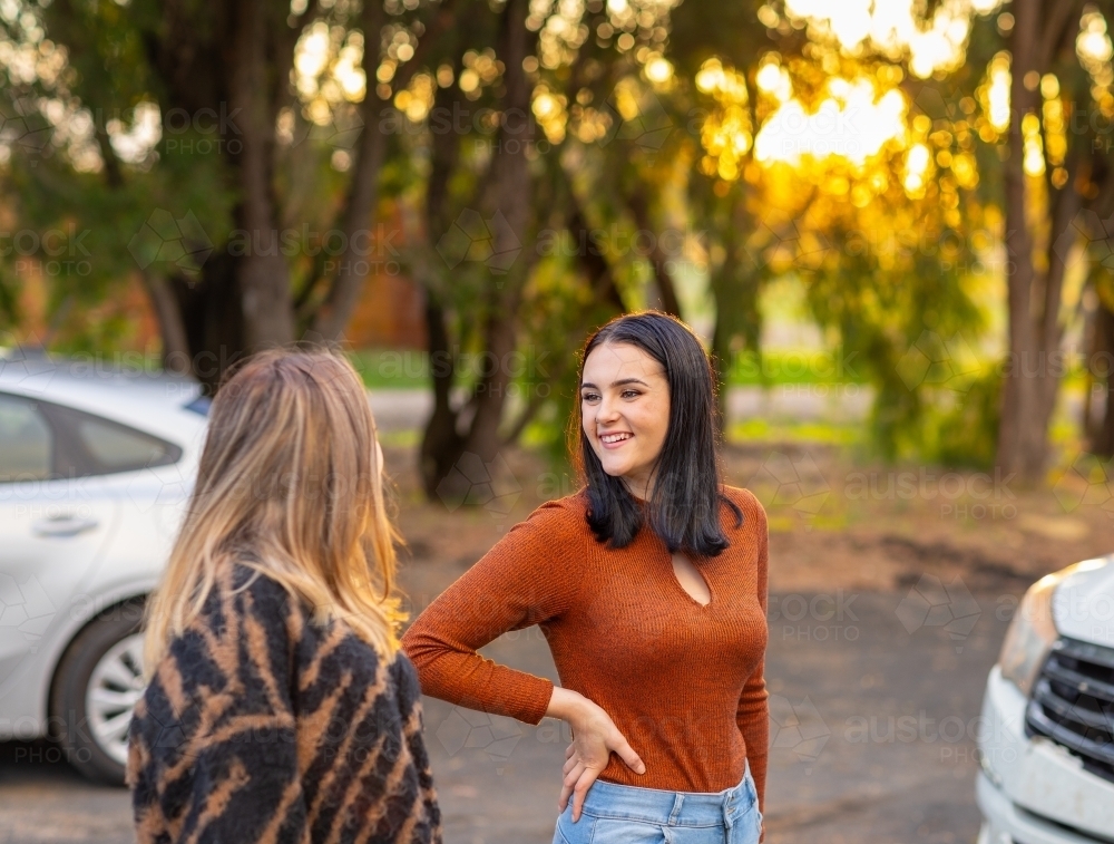 two teenagers outside near vehicles with trees in background - Australian Stock Image