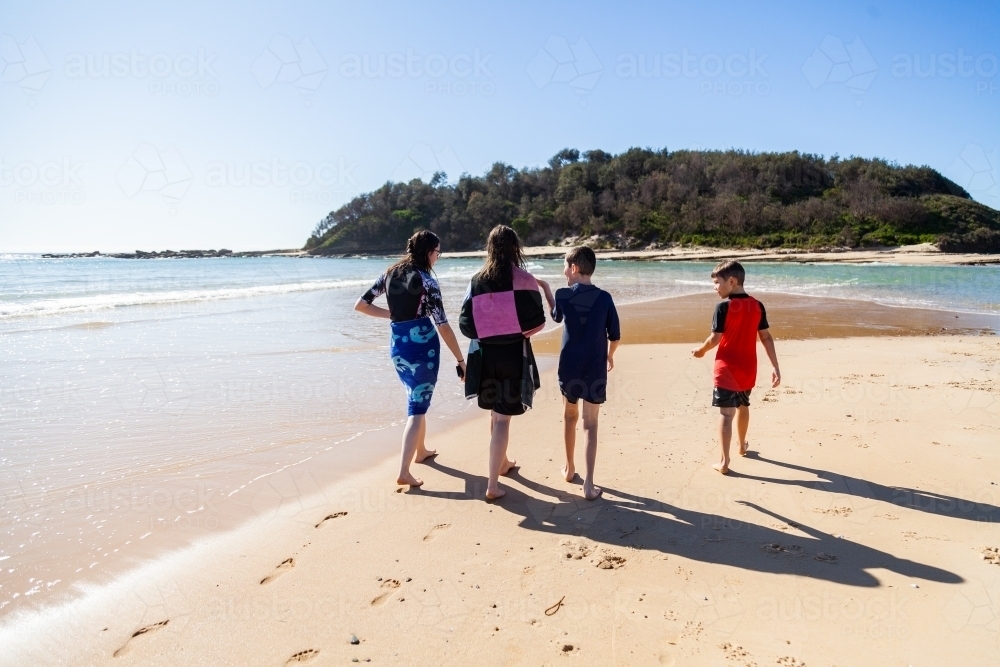 Two teens walking along beach with younger brothers - Australian Stock Image