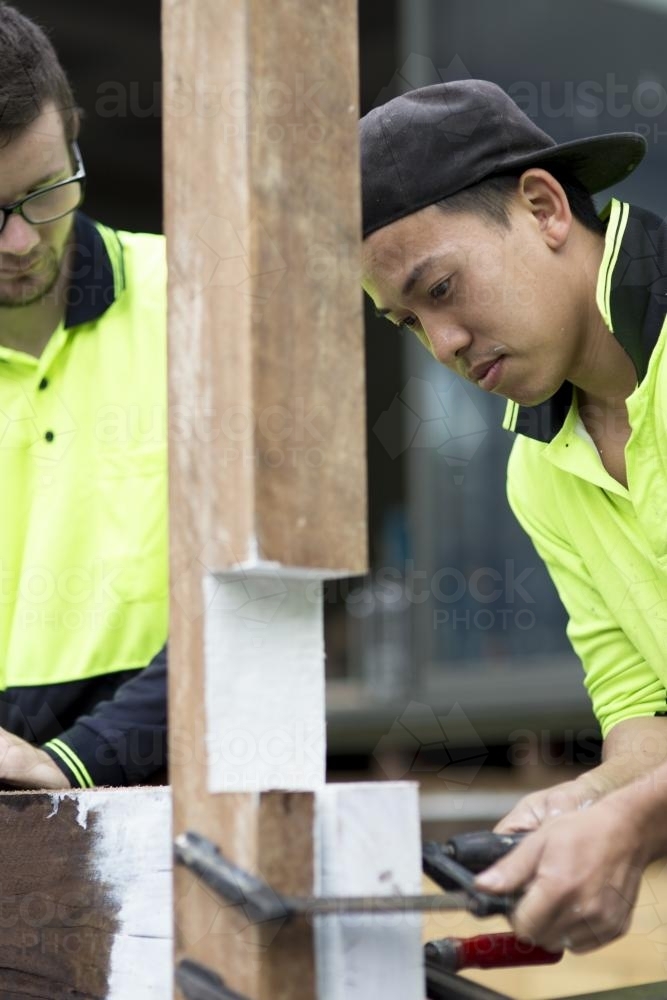 Two tradesmen adjust a wooden beam on a home renovation site. - Australian Stock Image