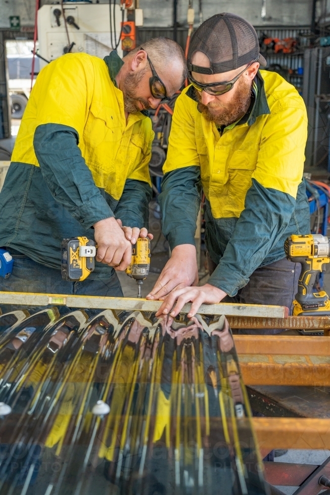 Two tradesmen cooperating to attach corrugated screening to an awning - Australian Stock Image