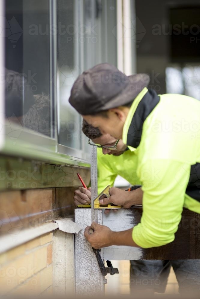 Two tradesmen making measurements on a wooden beam. - Australian Stock Image