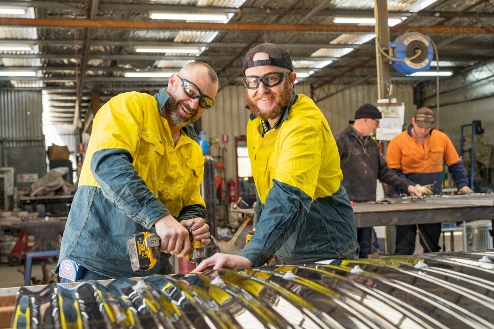 Two tradesmen smiling while holding down screening on a workbench - Australian Stock Image