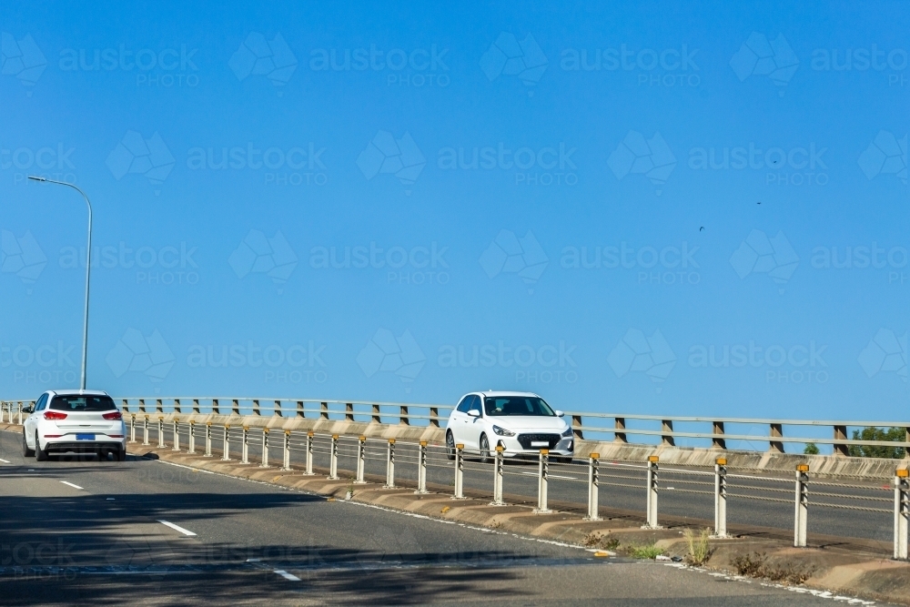 Two white cars passing each other on bridge with blue copy space above - Australian Stock Image
