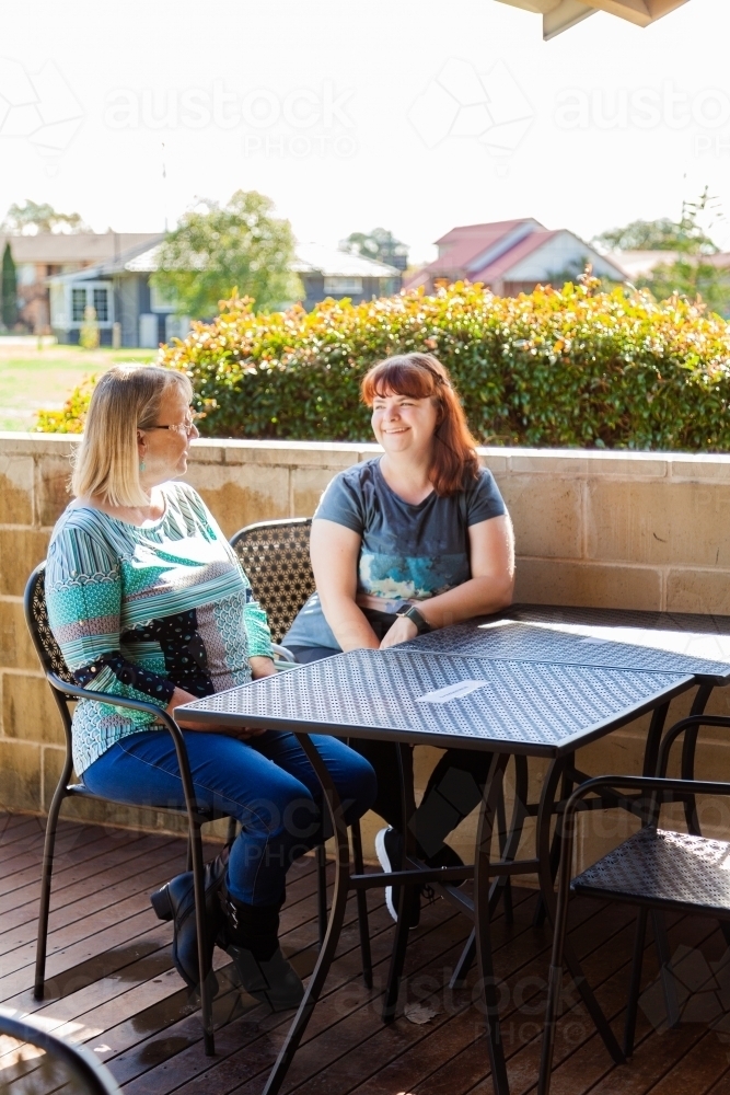 Two women chatting at a cafe, sitting outside in the sunlight - Australian Stock Image
