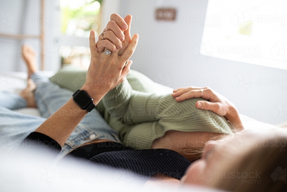 Female same sex couple  affectionately lying together on the bed, holding hands - Australian Stock Image