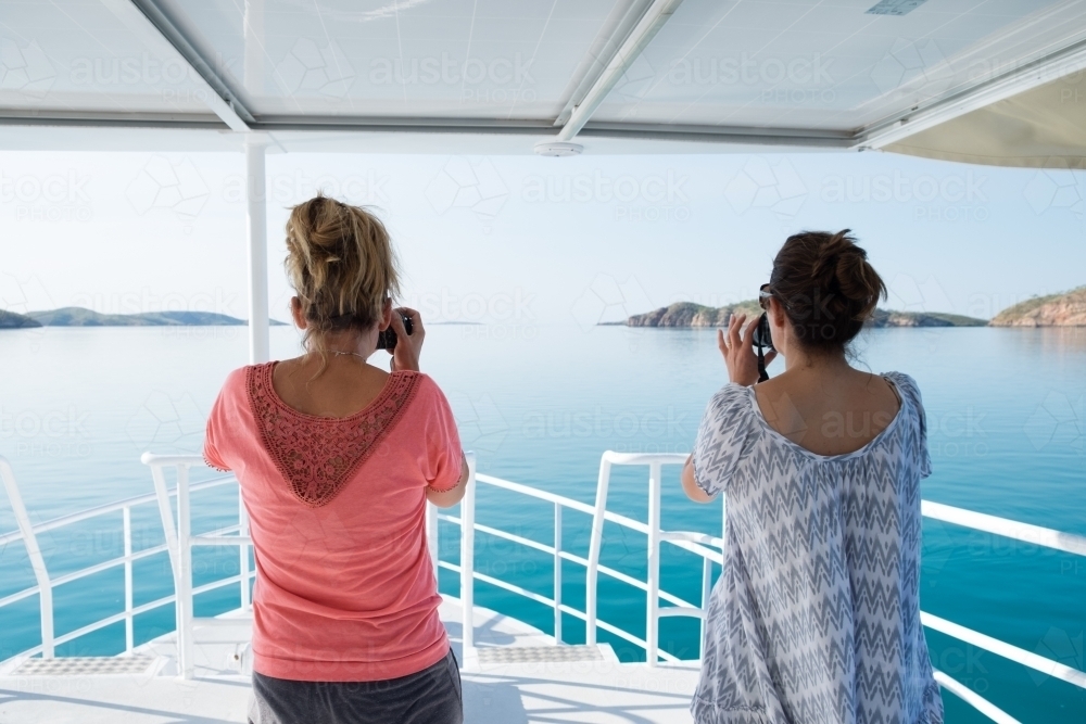 Two women on bow of pleasure cruiser boat on glassy still ocean whale watching taking photos - Australian Stock Image