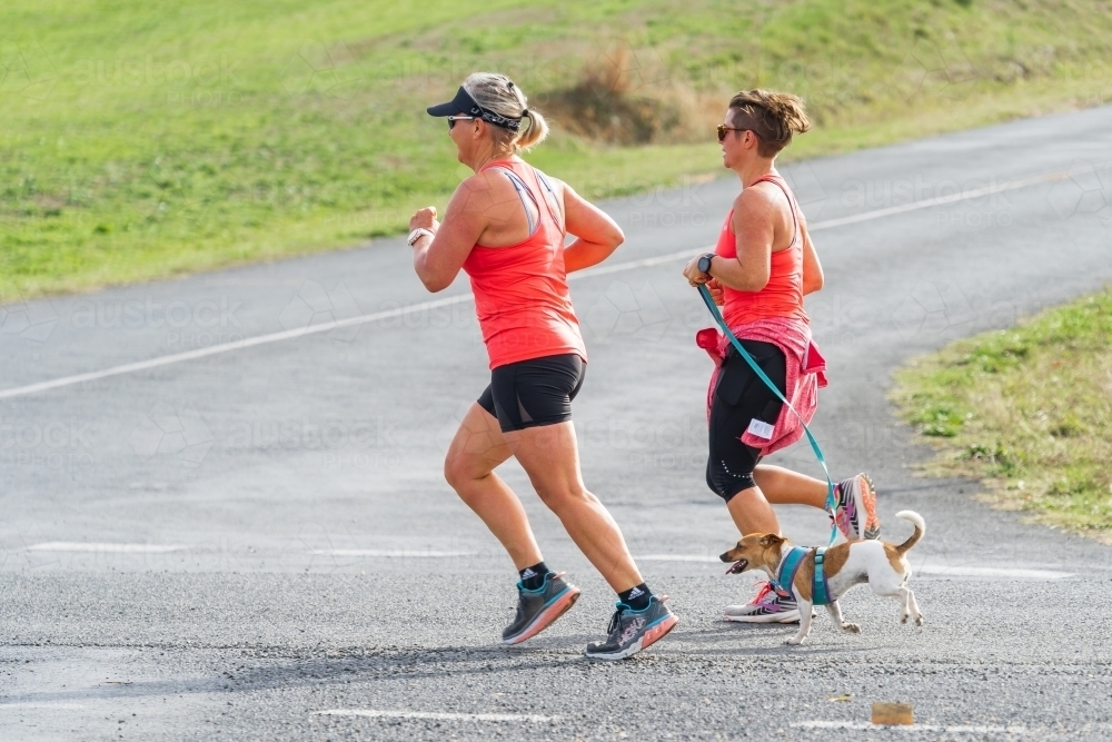 Two women running with a small dog on a neighbourhood street - Australian Stock Image