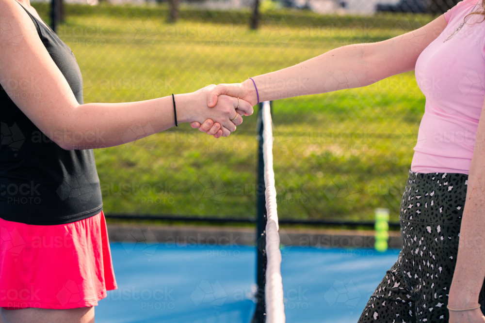 Two women shaking hands over tennis net on outdoor court - Australian Stock Image
