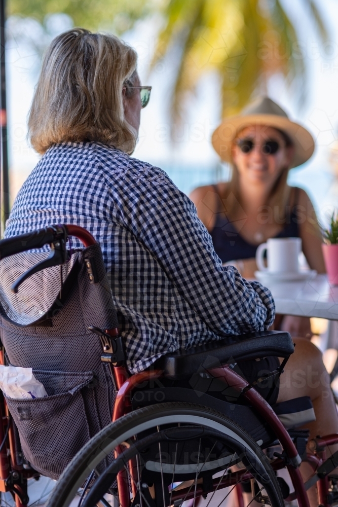 two women sitting at cafe with palm tree in background - Australian Stock Image