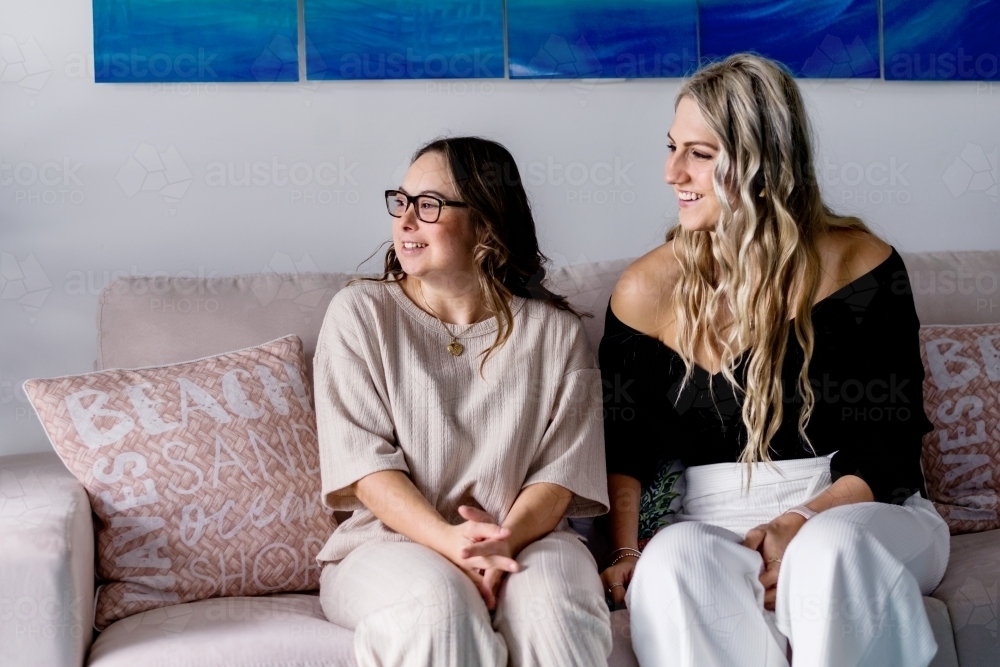 two women sitting on sofa, having a laugh. - Australian Stock Image