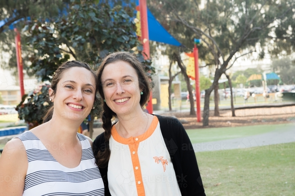 Two women smiling at the camera at the park. - Australian Stock Image