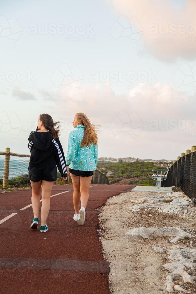 Two women walking along path by the coast at dusk - Australian Stock Image